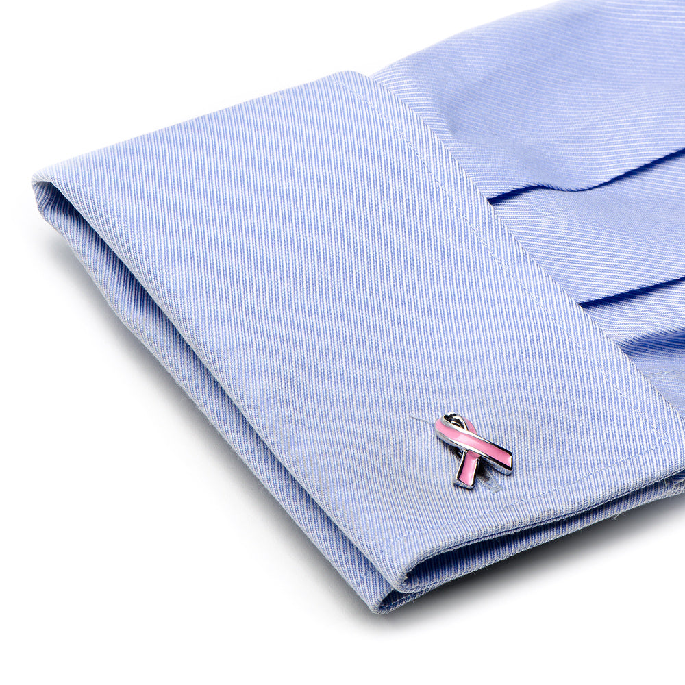 Folded light blue shirt with a pink breast cancer awareness ribbon pin on a white background