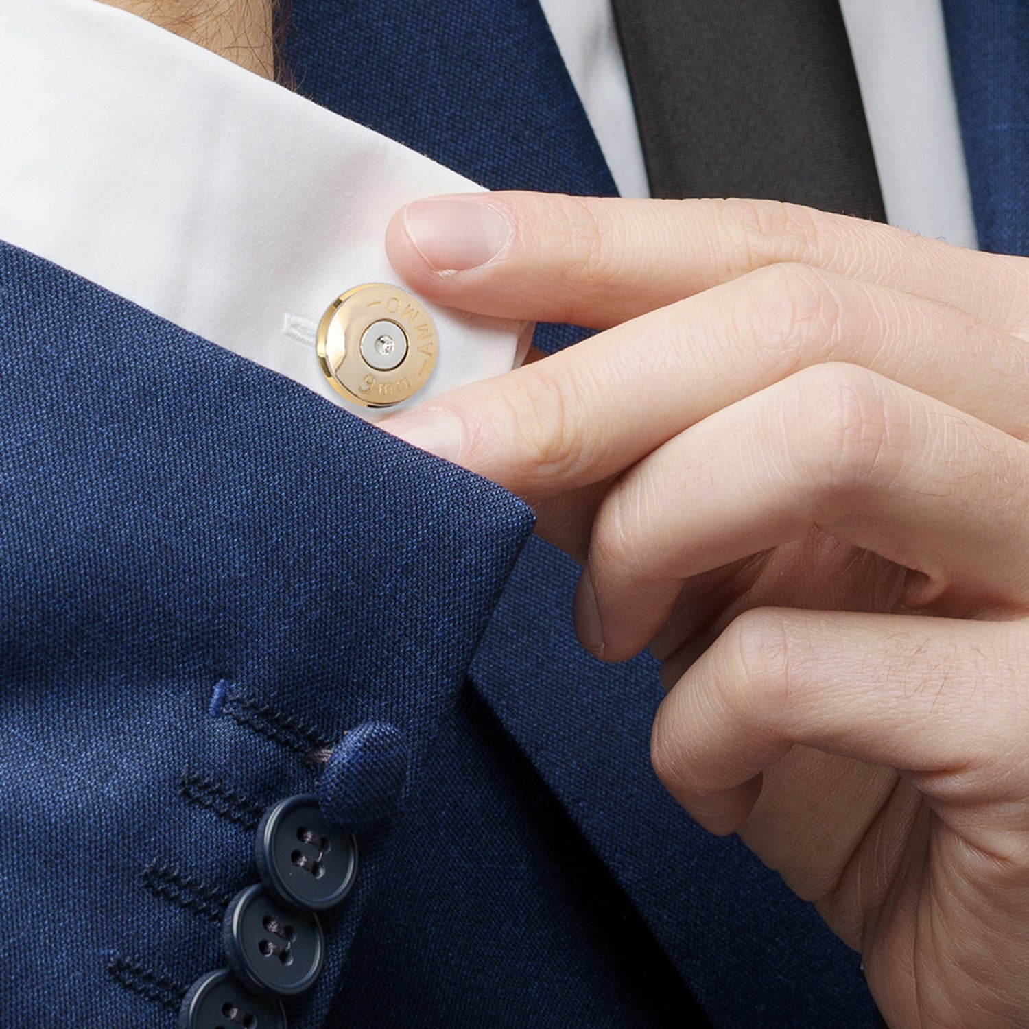 Hand adjusting a button on a blue jacket with a white shirt underneath.