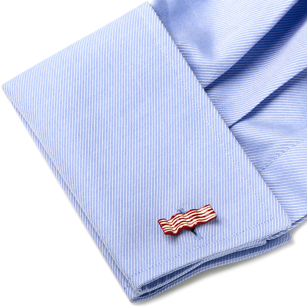 Folded light blue shirt with a flag-shaped cufflink on a white background