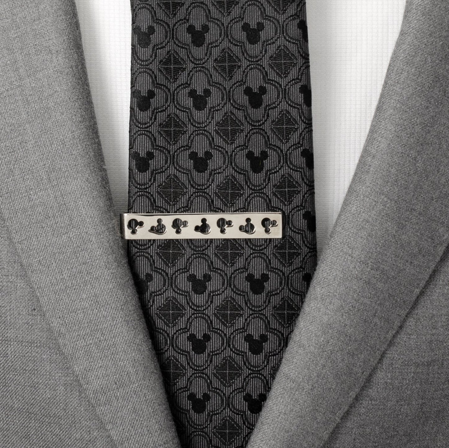 Gray suit jacket with a patterned tie and silver tie clip on a white shirt. Disney Mickey Mouse Silhouette Cutout Silver Tie Bar
