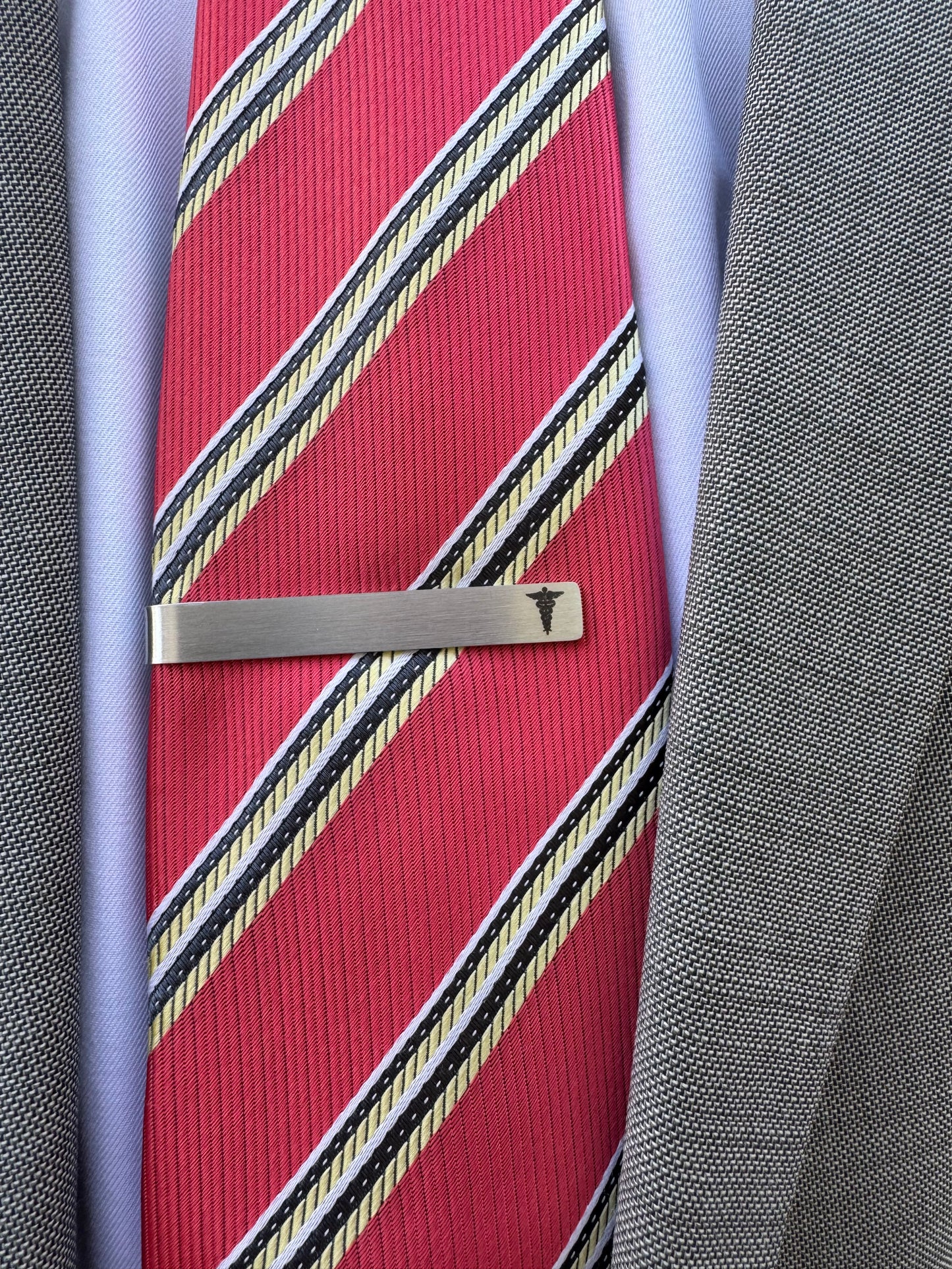Red striped tie with a silver tie clip on a gray fabric background