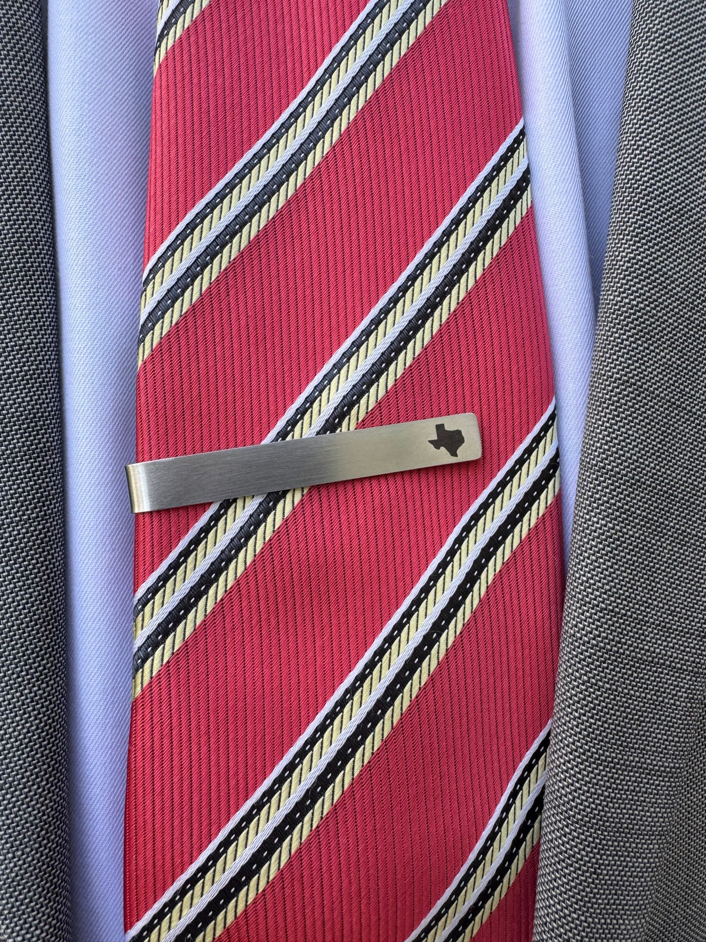 Red striped tie with a silver tie clip on a textured surface