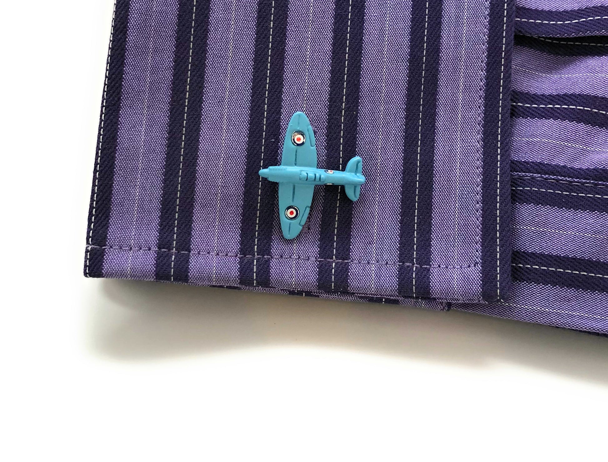 Close-up of a blue airplane pin on a striped shirt sleeve. Baby blue WWII Spitfire airplane cufflinks with silver backing – vintage aviation-inspired men’s jewelry from JayPins