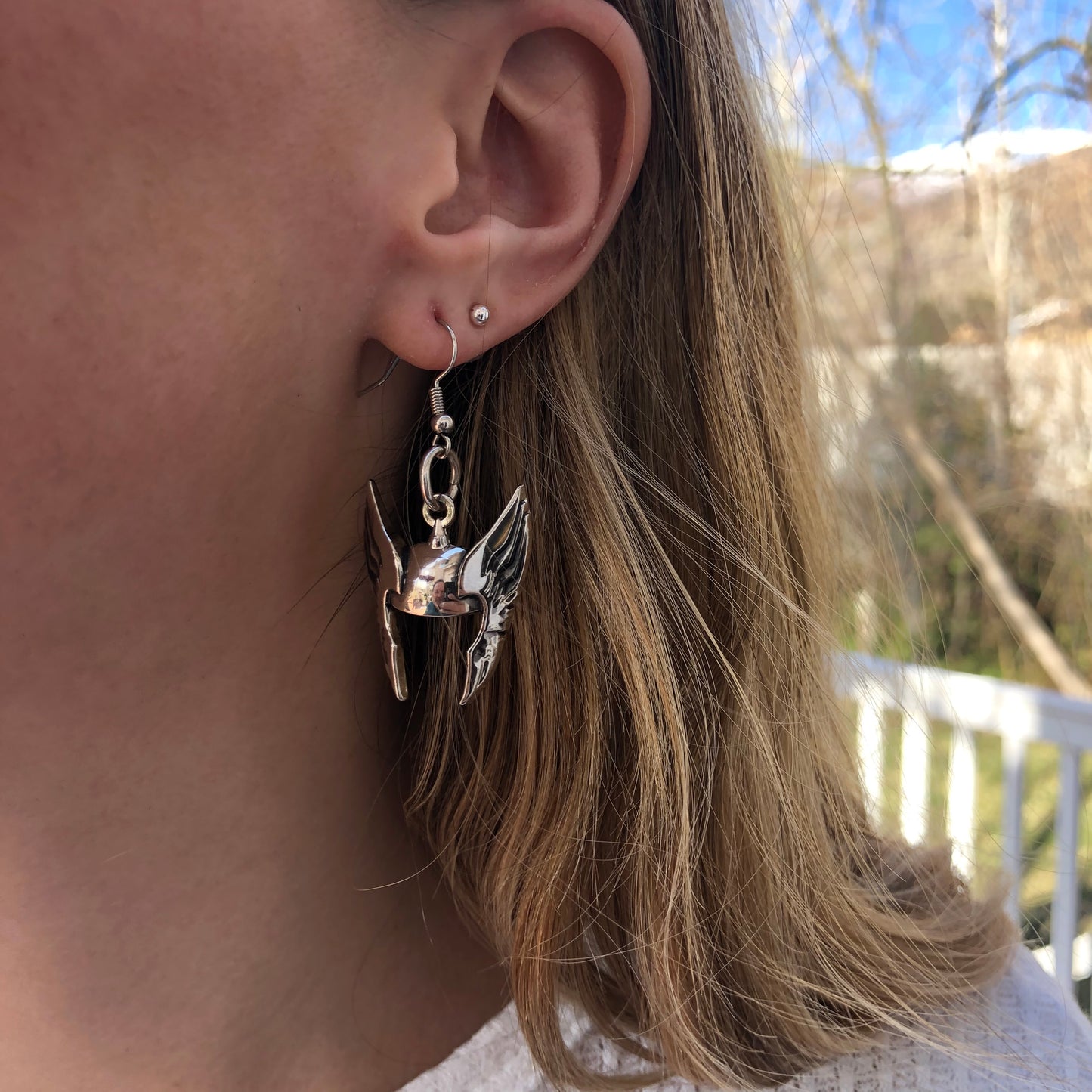 Close-up of an ear with a silver earring, hair partially covering it, outdoors.