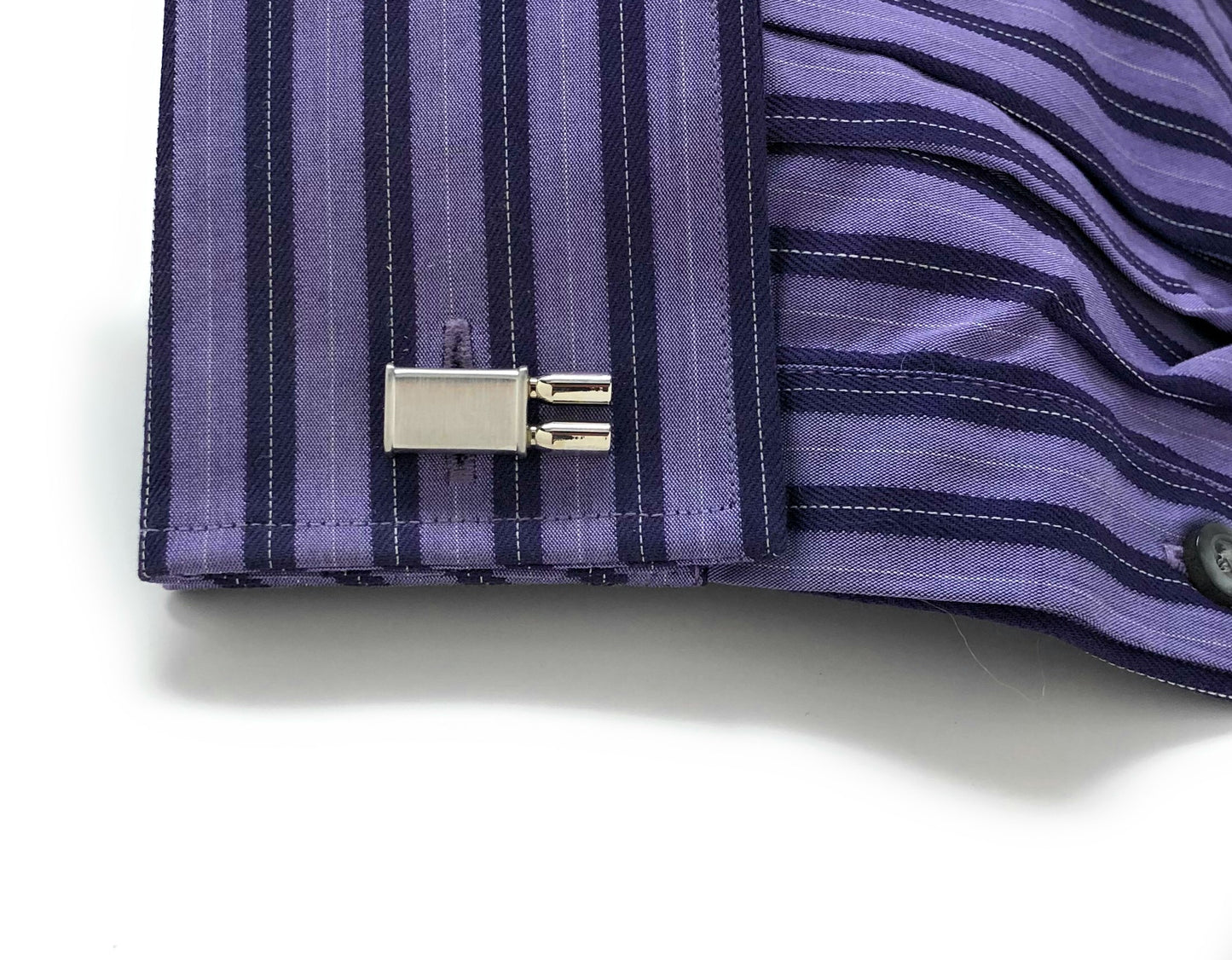 Close-up of a purple striped shirt cuff with a button and cufflink on a white background