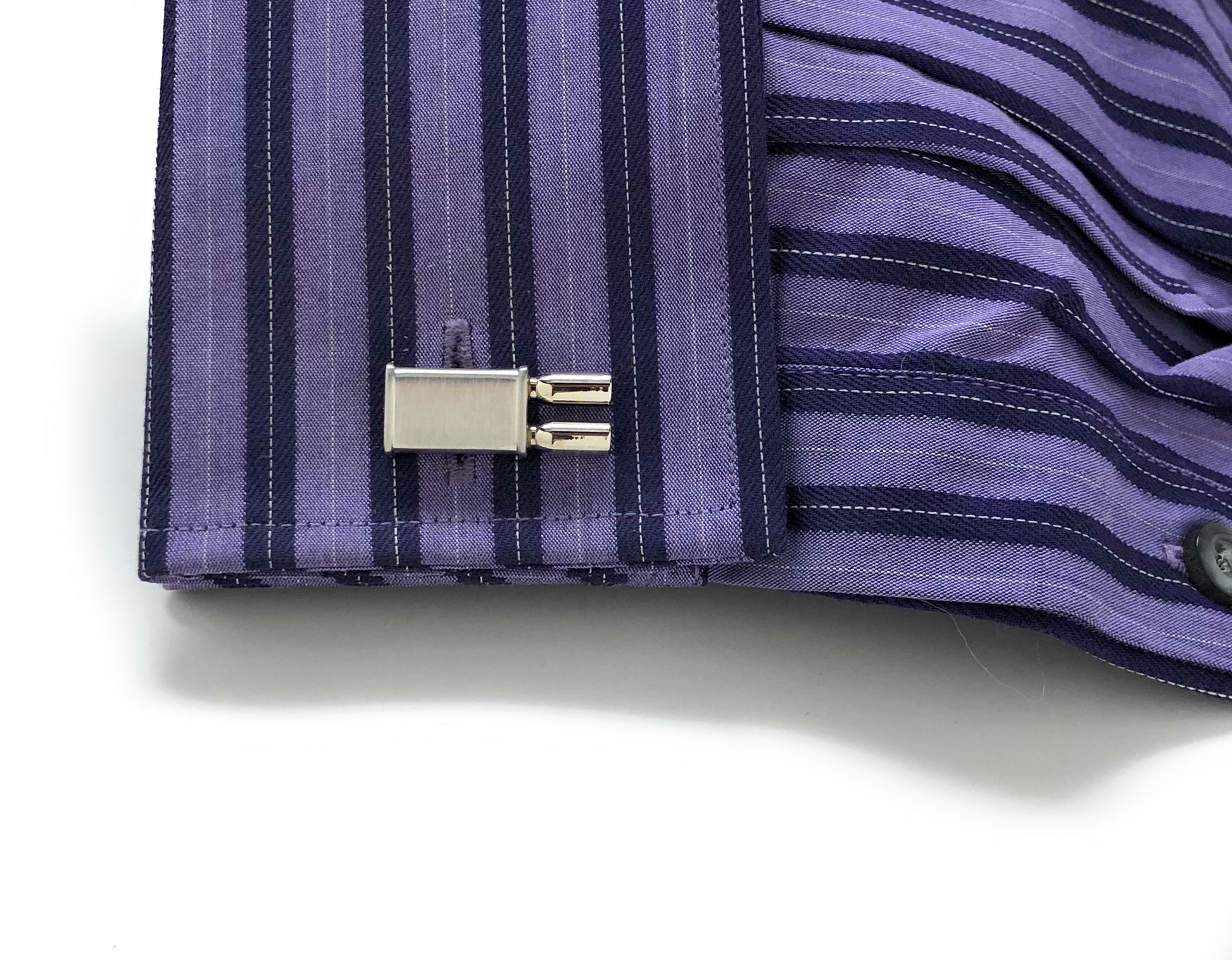 Close-up of a purple striped shirt cuff with a button and cufflink on a white background
