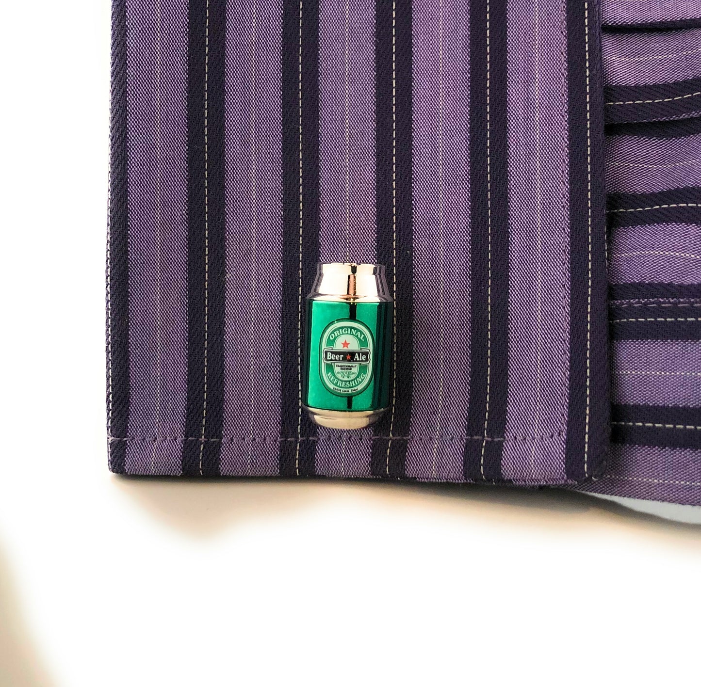 Green beer can-shaped object on a purple striped fabric background