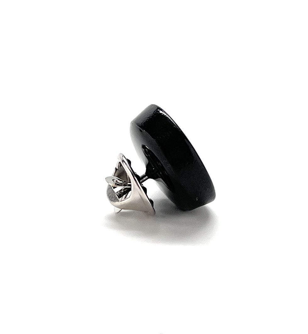 A black cast iron frying pan lapel pin with a silver rhodium plated design and white enamel detailing, displayed alongside a close-up of the pin's backside showing the butterfly clasp.