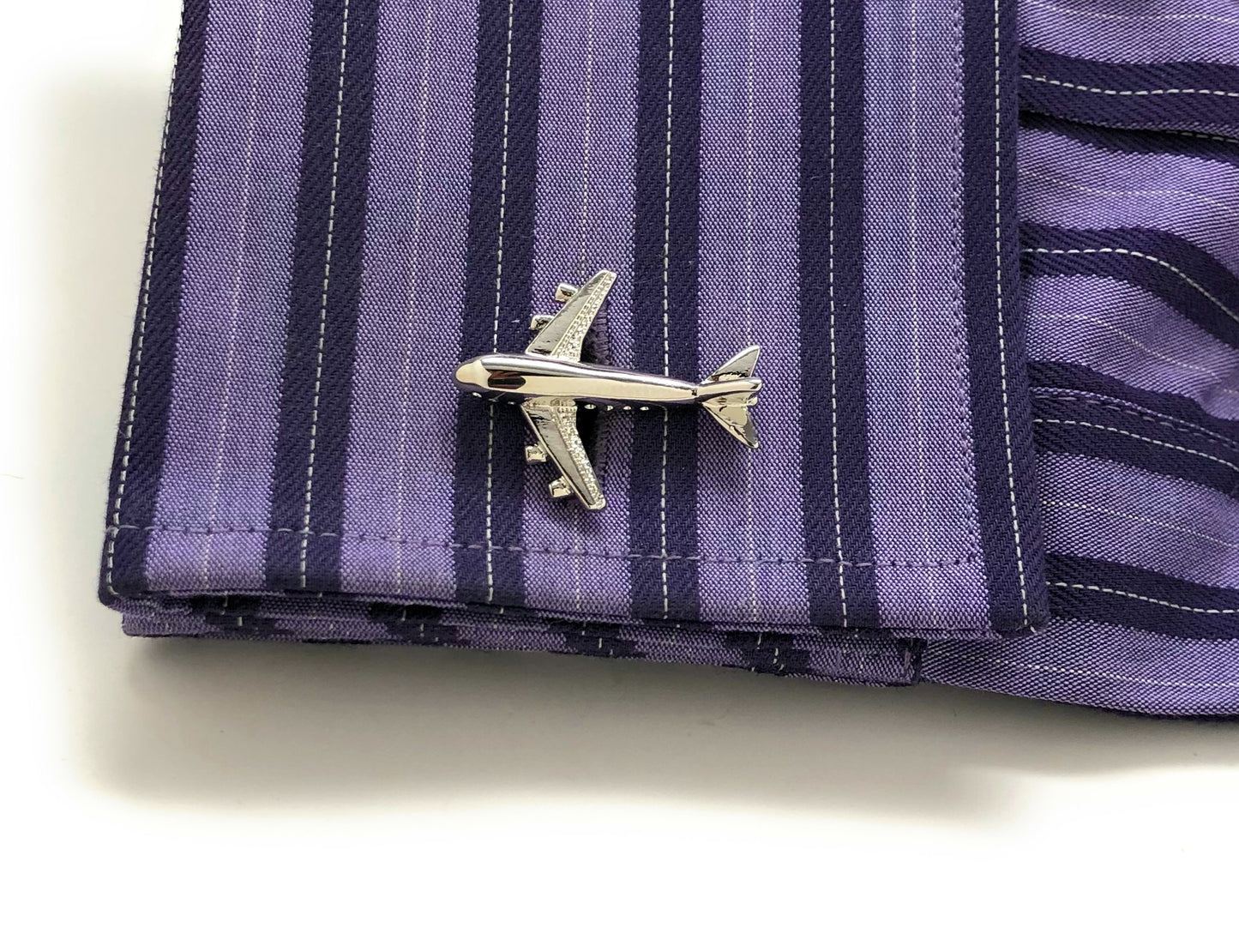 Silver airplane pin on a purple striped fabric background