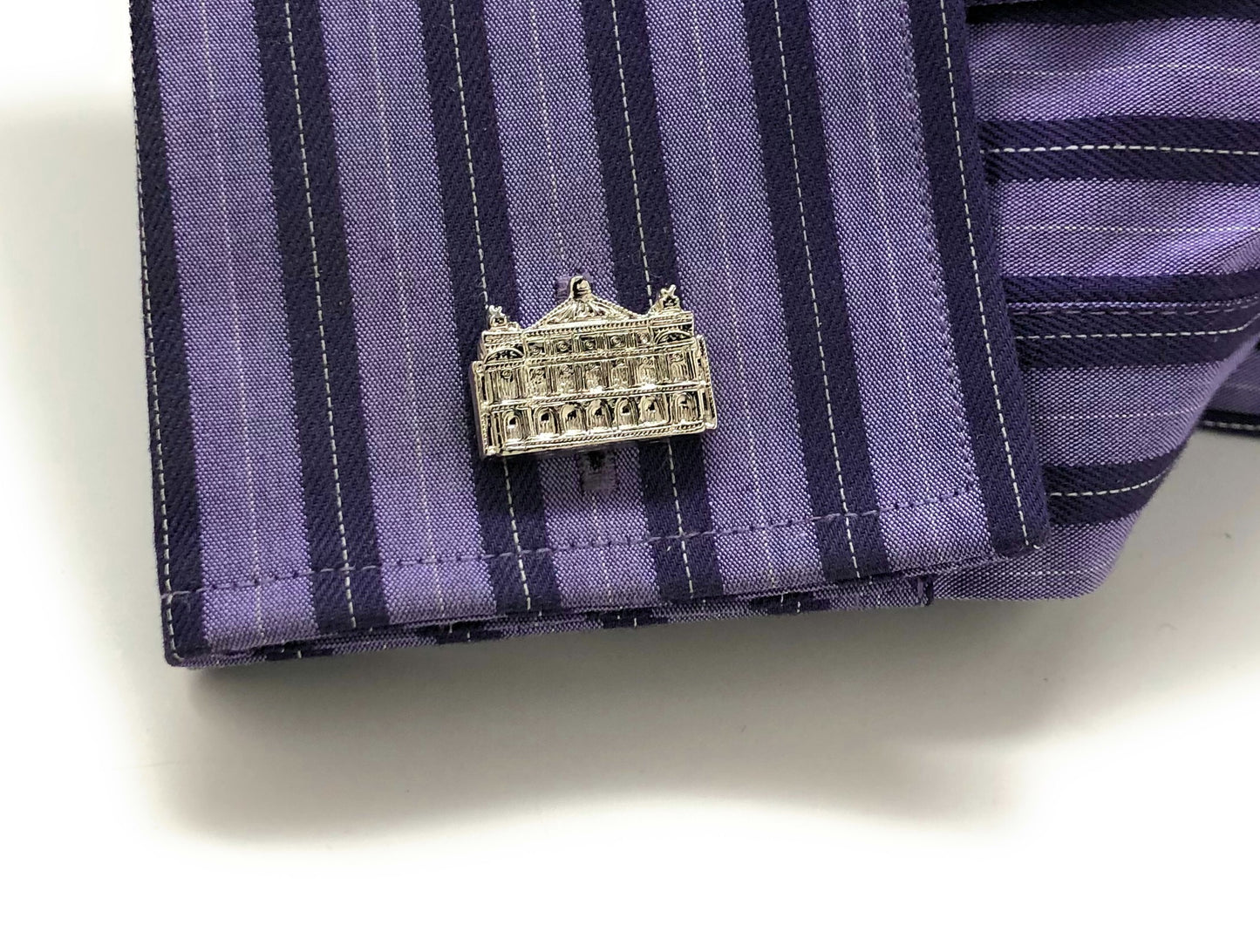 Silver building-shaped pin on a purple striped fabric background