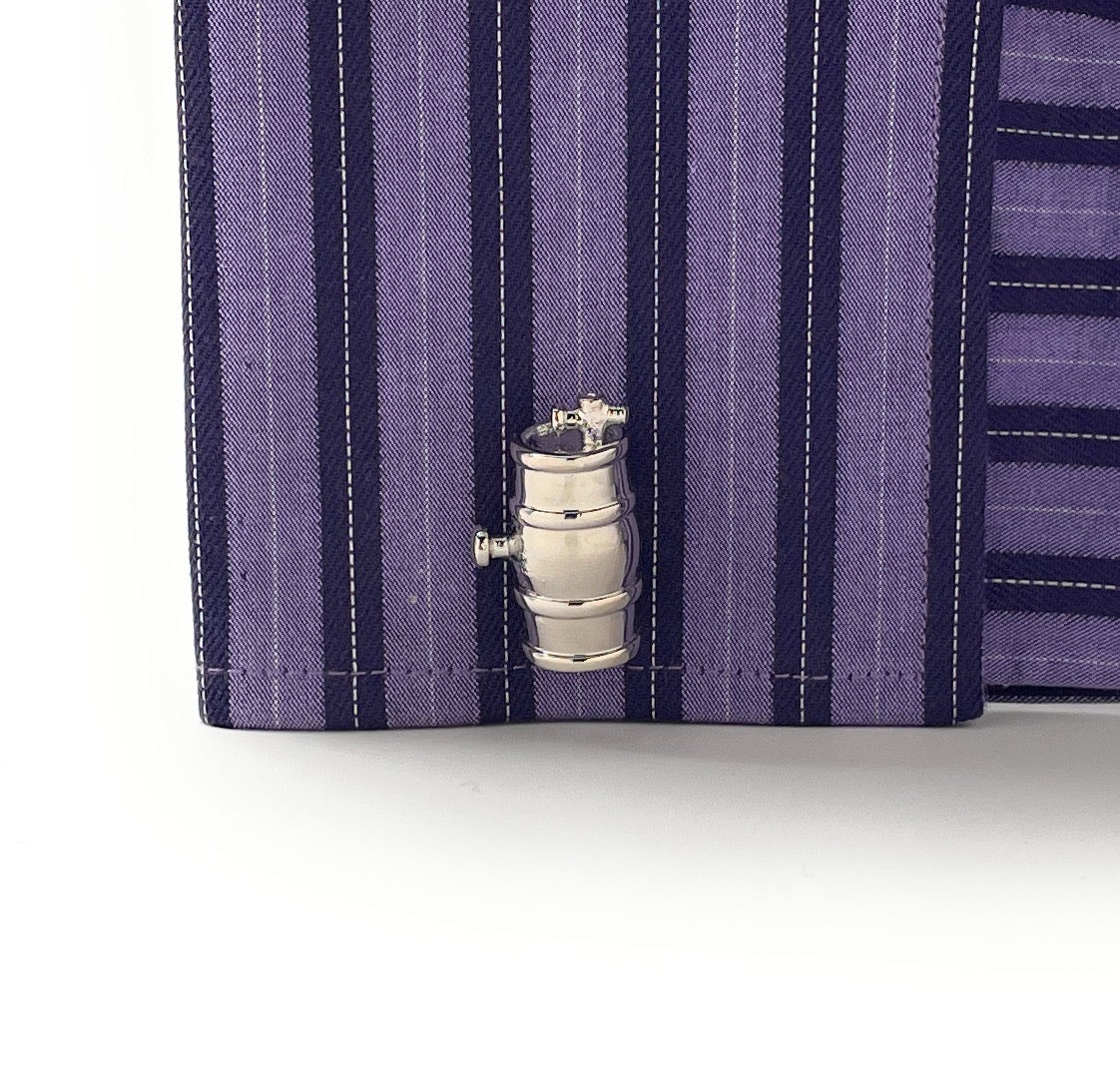 Close-up of a purple striped shirt with a metal valve charm on a white background