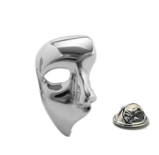 A silver-colored lapel pin in the shape of a mask, with a shiny finish and a butterfly back.
