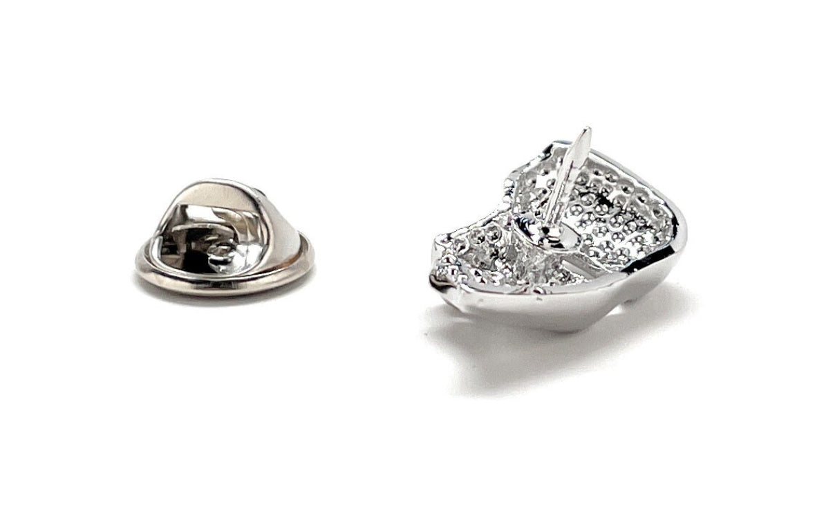 A silver-colored lapel pin in the shape of a mask, with a shiny finish and a butterfly back.