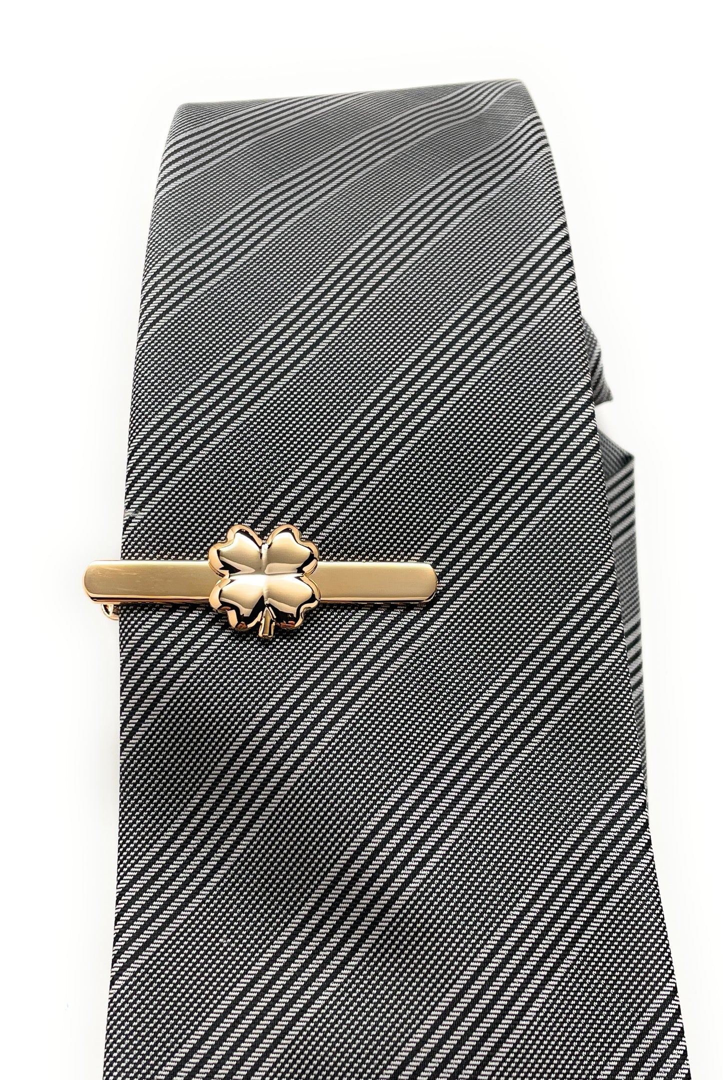 Gold shamrock tie clip on a striped tie against a white background
