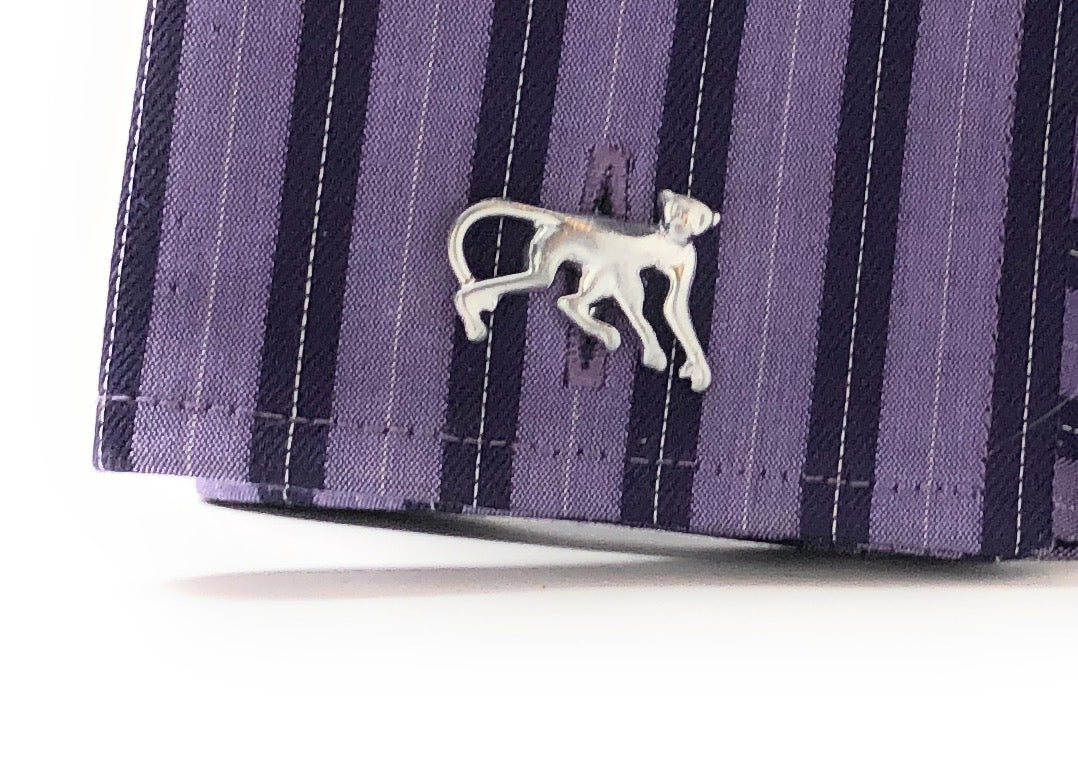 Silver monkey-shaped brooch on a purple striped fabric background