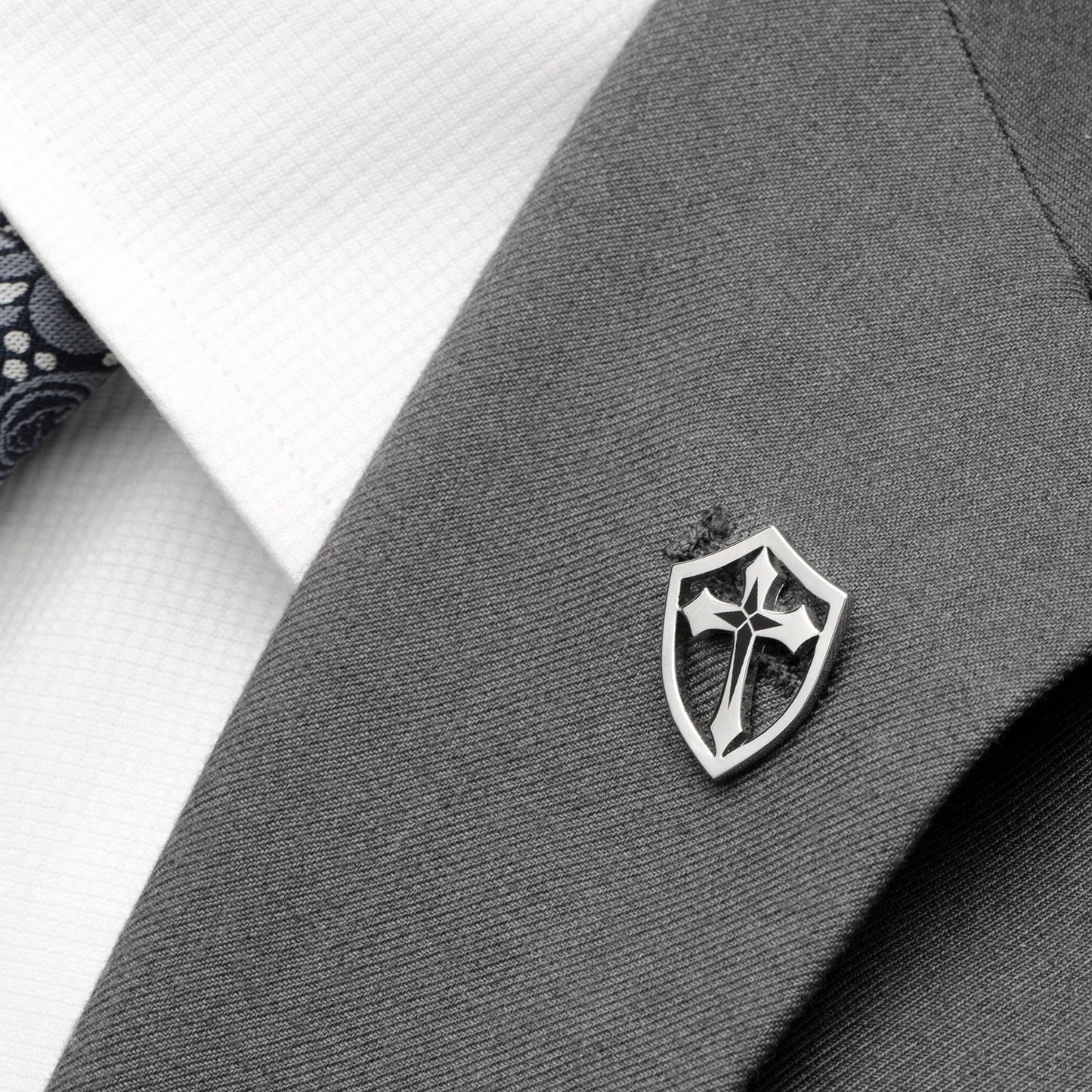 Silver emblem on a gray suit jacket with a white shirt and black tie.
