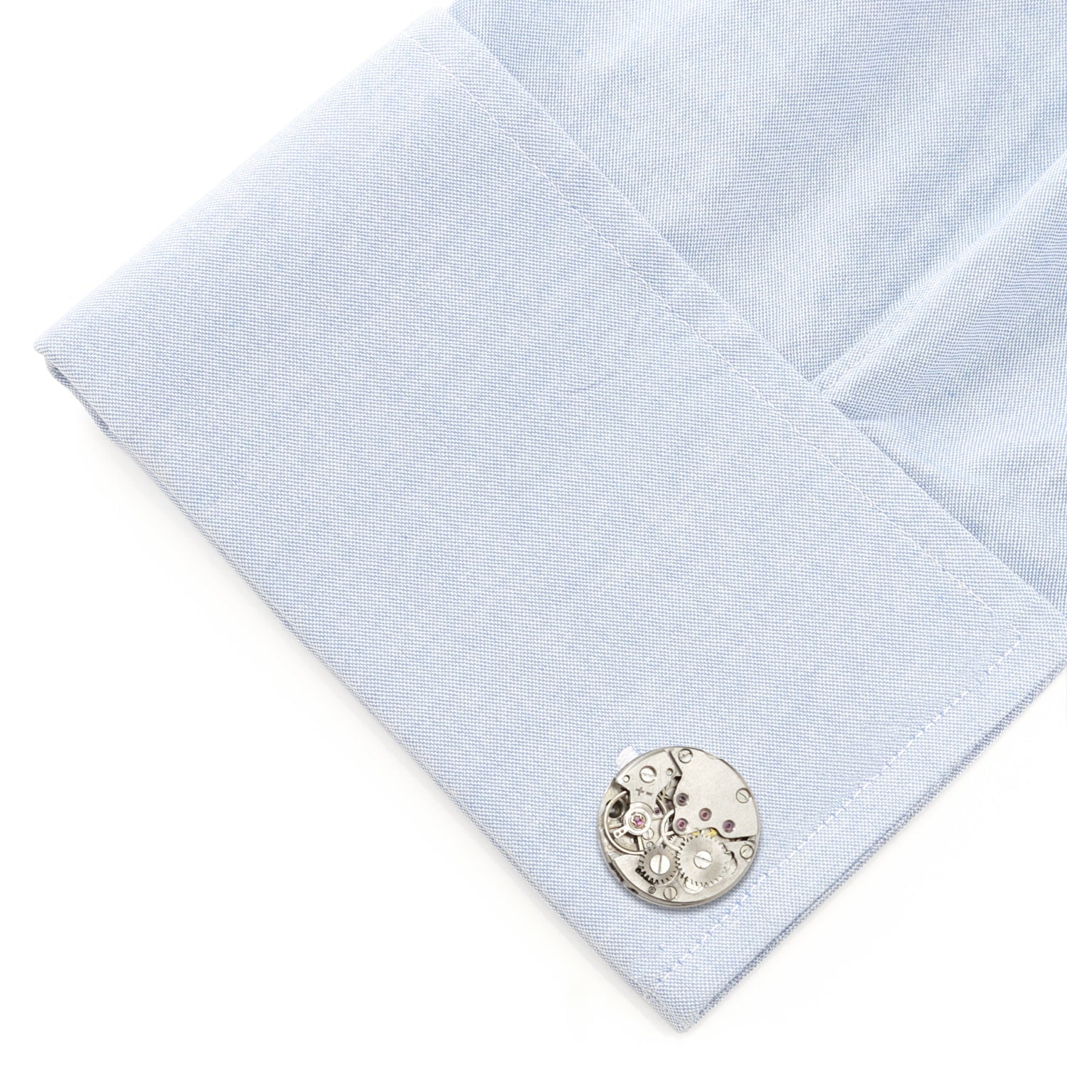 Cufflink on a light blue dress shirt with a white background
