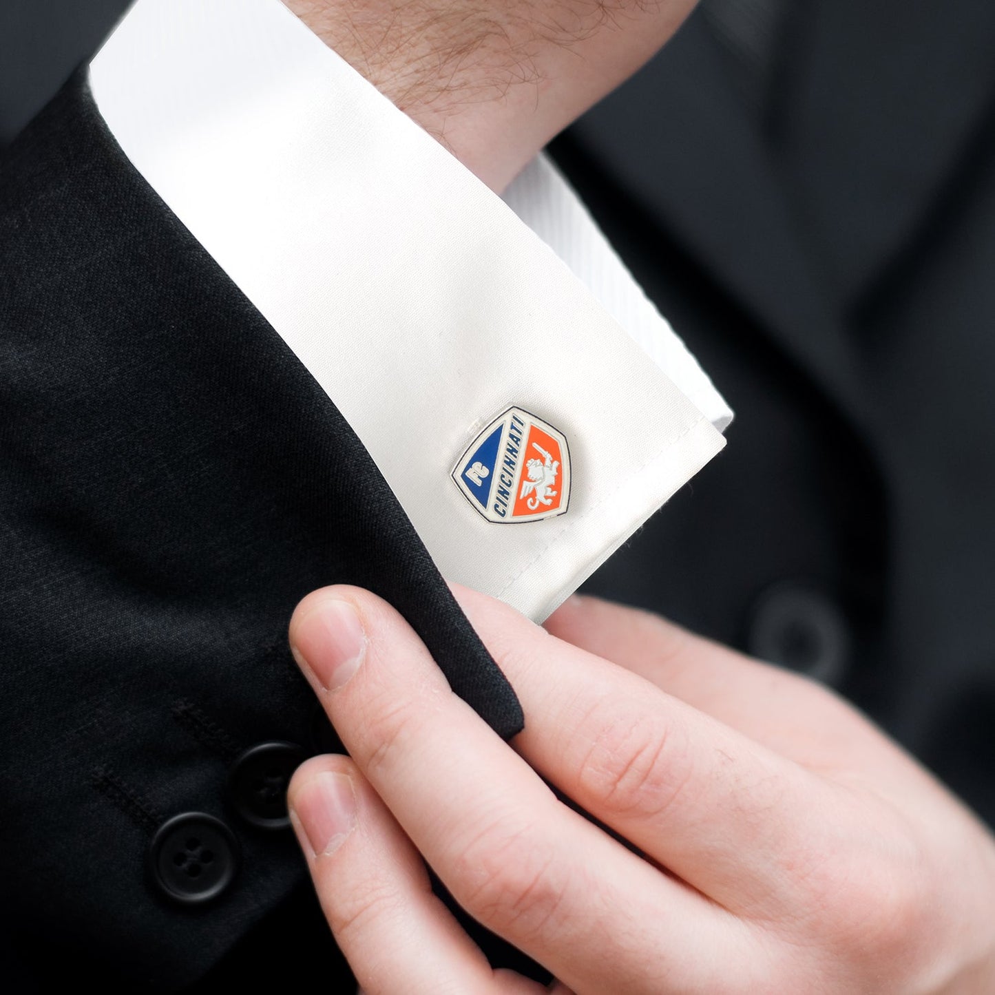 Close-up of a suit cuff with a logo being adjusted by a hand.