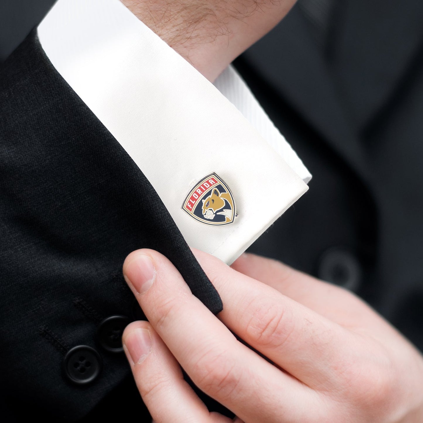 Cufflink with a brand logo being adjusted on a suit cuff
