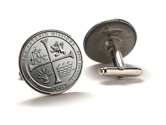 A pair of silver-colored cufflinks with an engraved design representing the San Antonio Missions National Historical Park, featuring a cross and a building.
