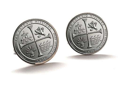 A pair of silver-colored cufflinks with an engraved design representing the San Antonio Missions National Historical Park, featuring a cross and a building.