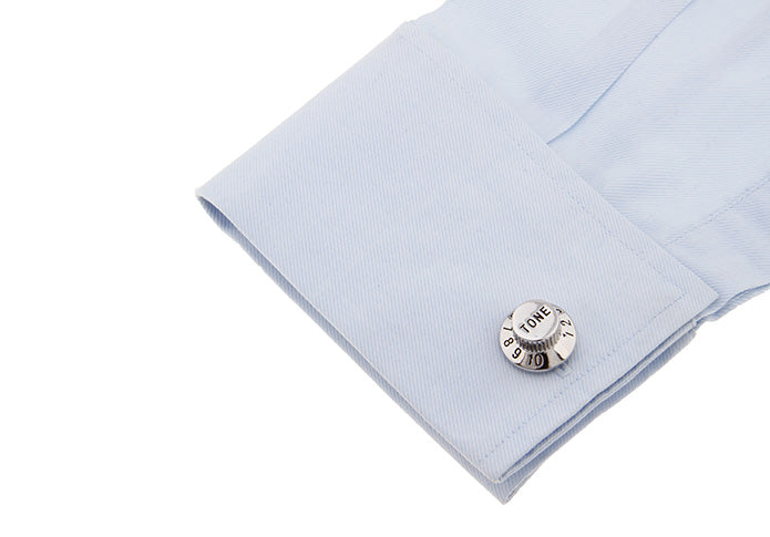 A close-up of a light blue dress shirt cuff with a single silver-toned tone-up cufflink on a plain white background.