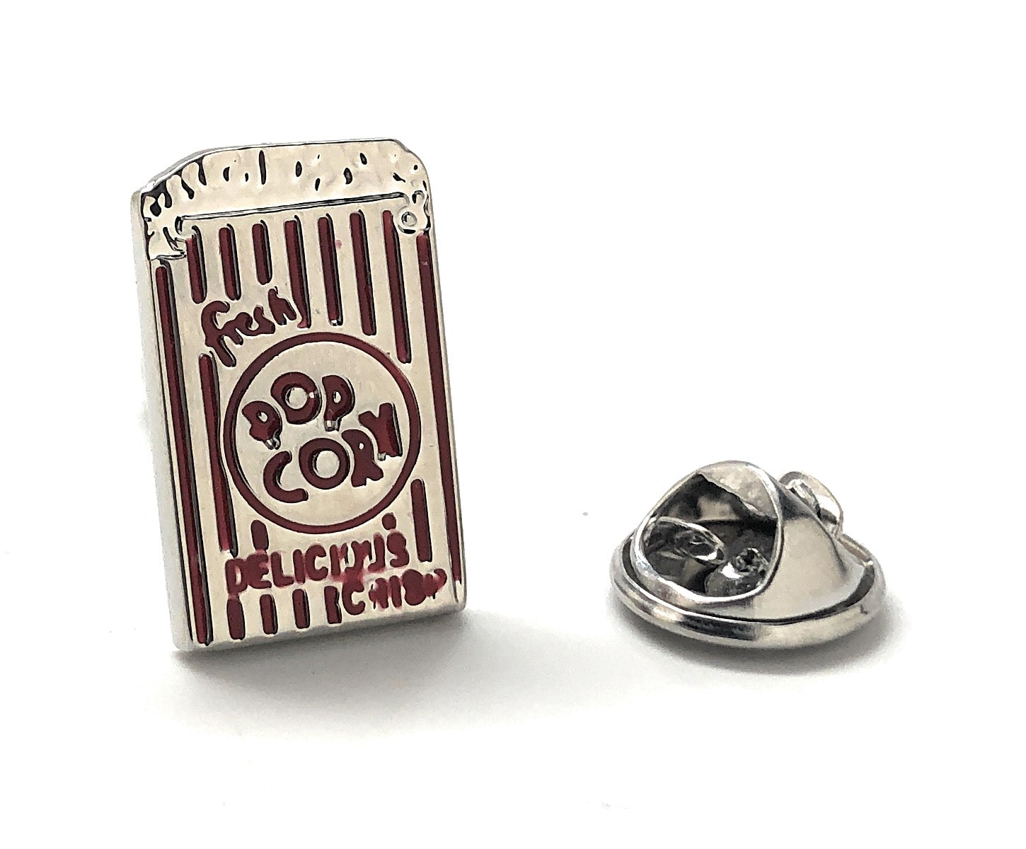 A silver lapel pin shaped like a popcorn container with red enamel text reading 'FRESH POPCORN DELICIOUS INSPIRATION' and a small depiction of popcorn.