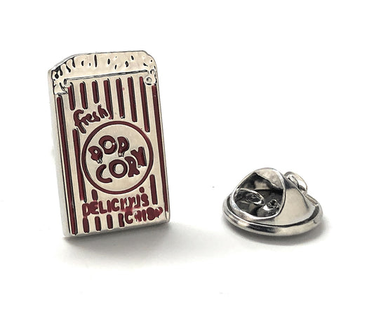 A silver lapel pin shaped like a popcorn container with red enamel text reading 'FRESH POPCORN DELICIOUS INSPIRATION' and a small depiction of popcorn.