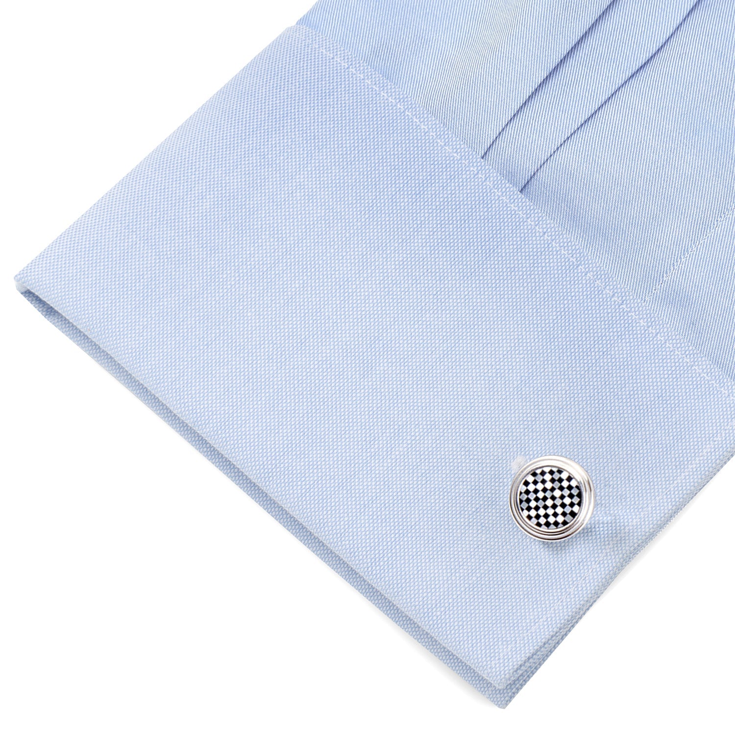 Close-up of a light blue shirt cuff with a silver and black checkered cufflink.