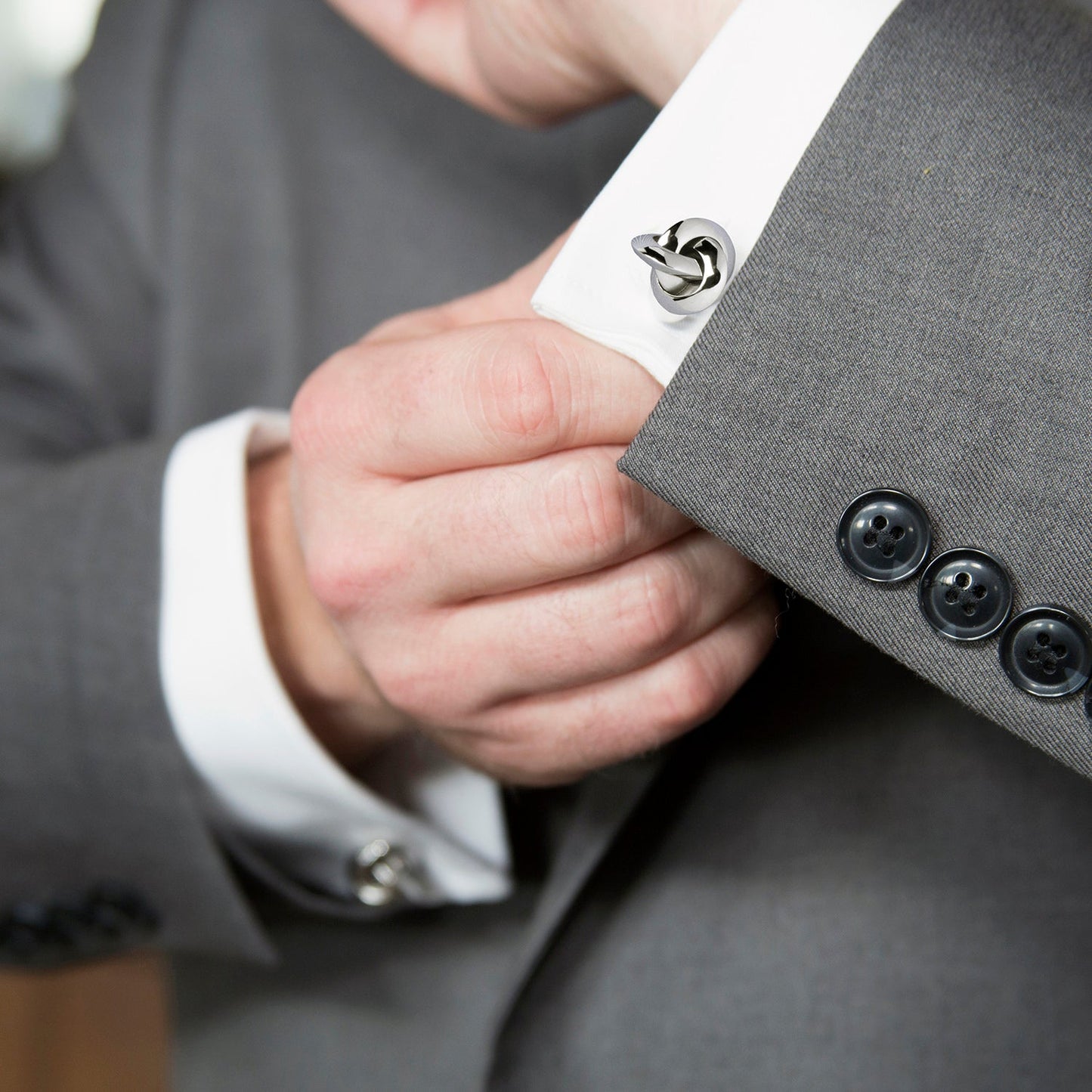 Close-up of a person adjusting a cufflink on a gray suit jacket.