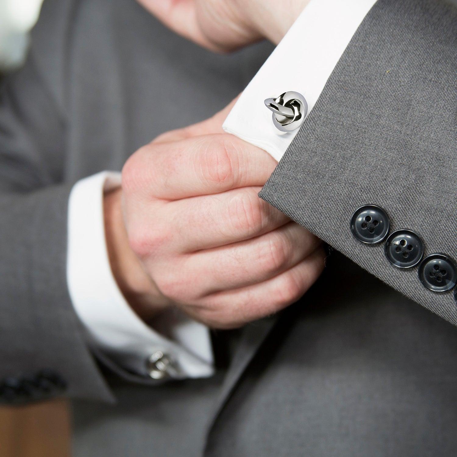 Close-up of a person adjusting a cufflink on a gray suit jacket.