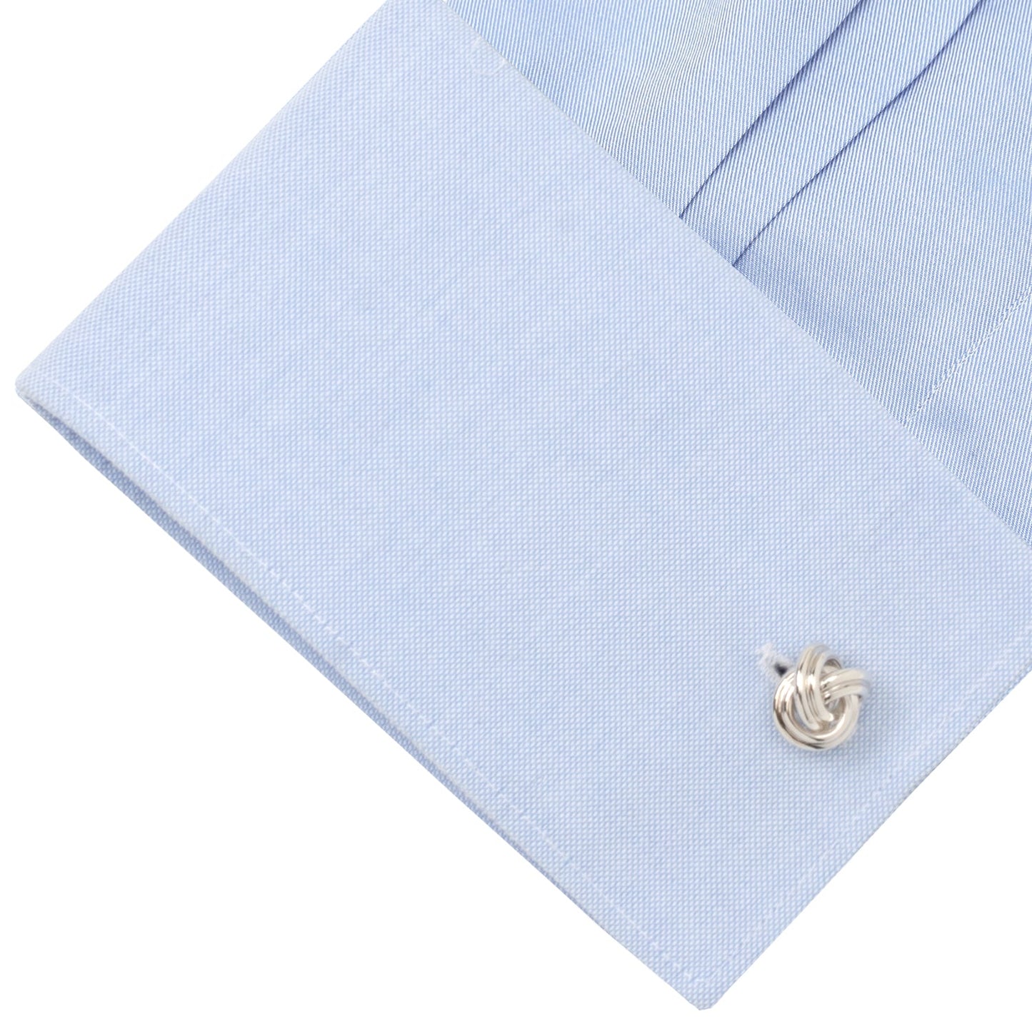Close-up of a light blue dress shirt with a silver cufflink on a white background