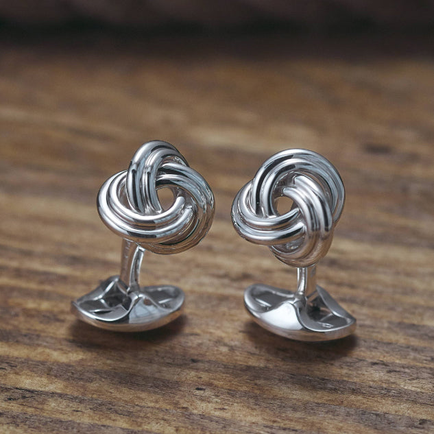 Pair of silver knot cufflinks on a wooden surface