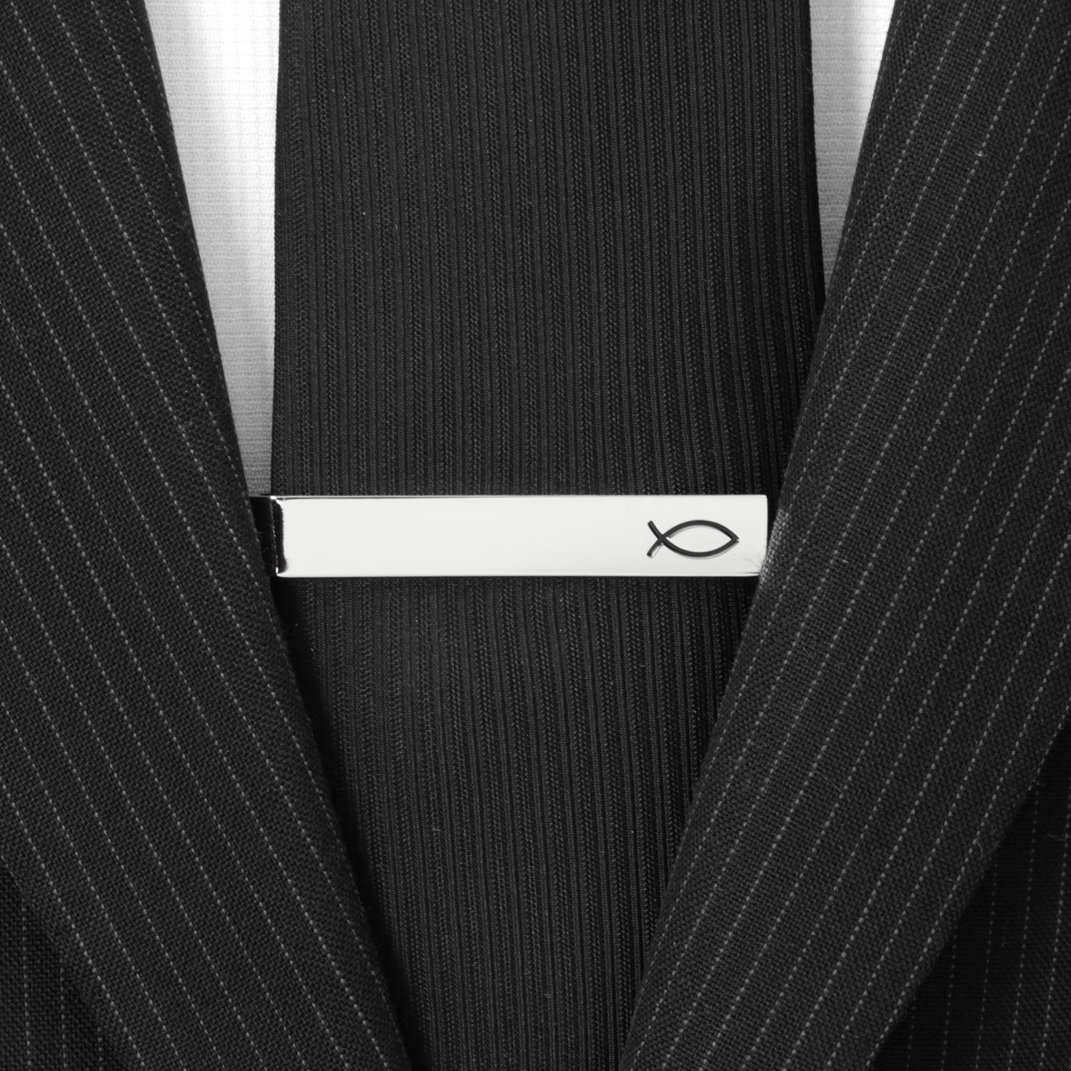 Black tie with a silver tie clip featuring a fish symbol on a black pinstripe suit.