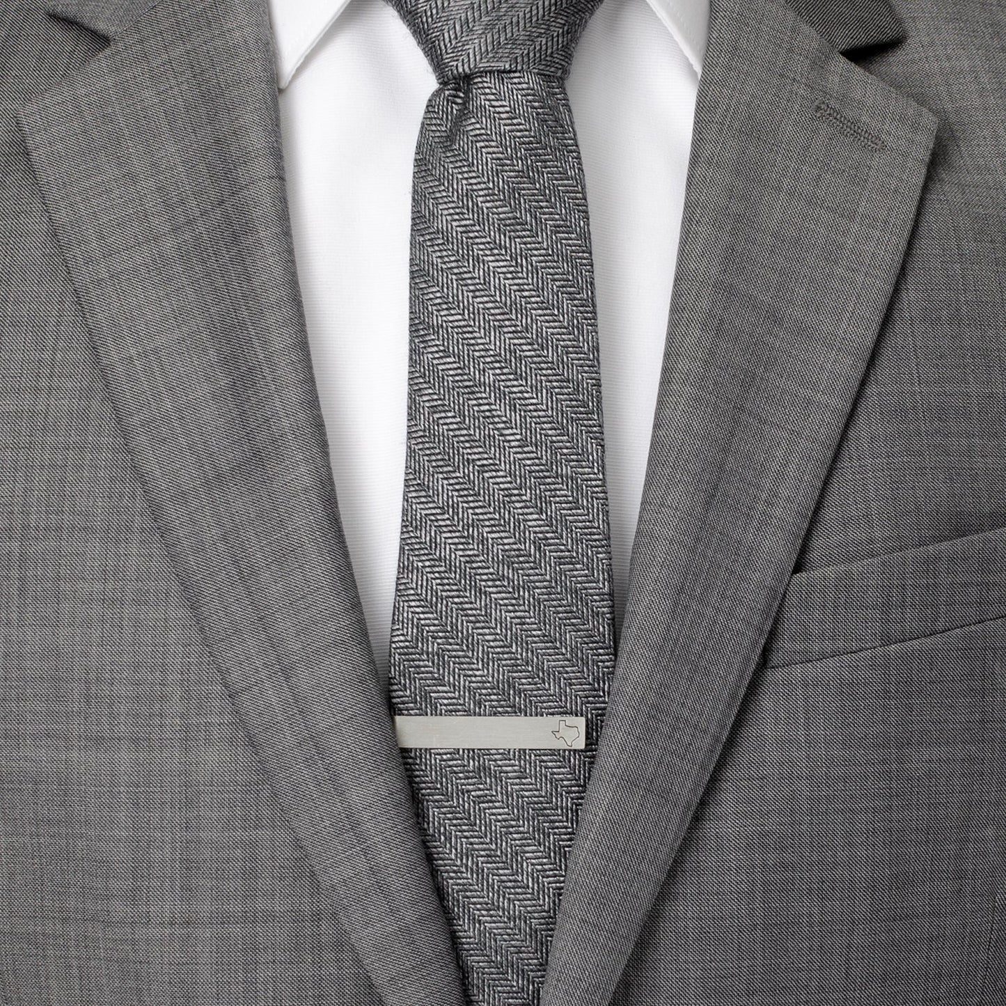 Gray suit with a patterned tie and silver tie clip on a white background