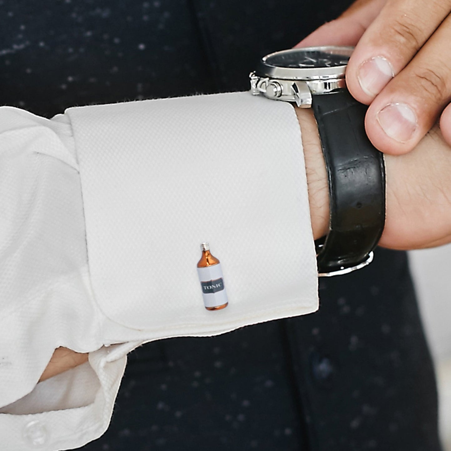 Cufflink resembling a bottle on a person's cuff with a watch on their wrist.