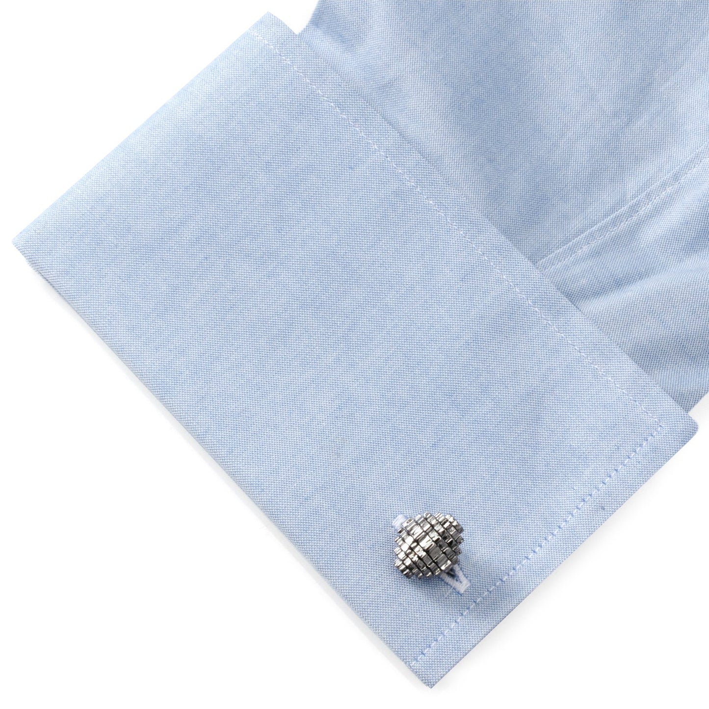 Close-up of light blue shirt cuff with a textured silver cufflink on a white background