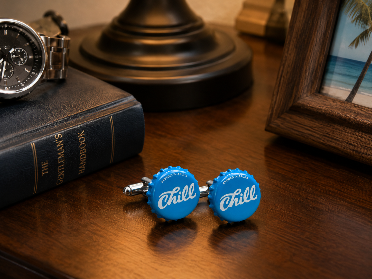 Authentic Aruba Chill Beer bottle cap cufflinks displayed on a wooden nightstand beside a watch, book, and tropical vacation photo.
