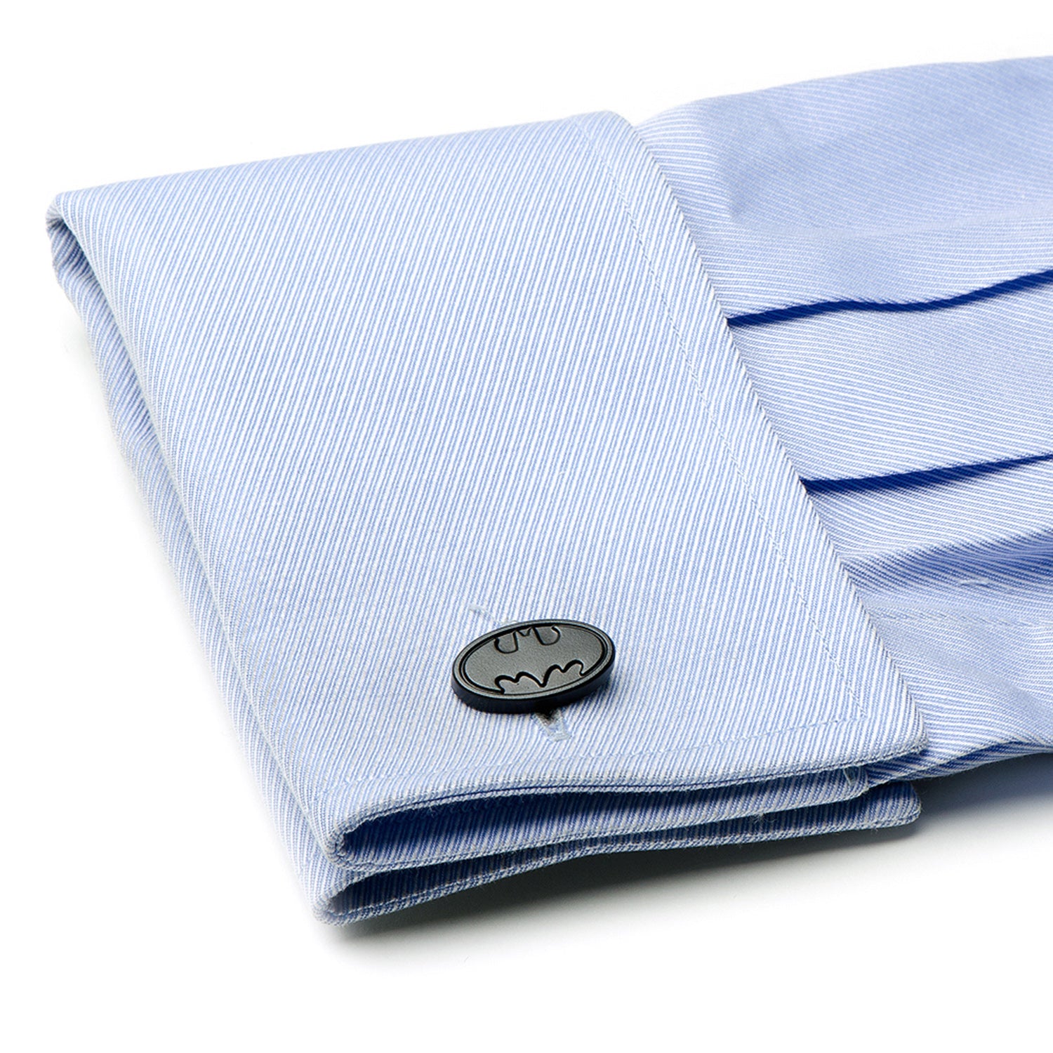 Folded light blue shirt with a Batman logo cufflink on a white background