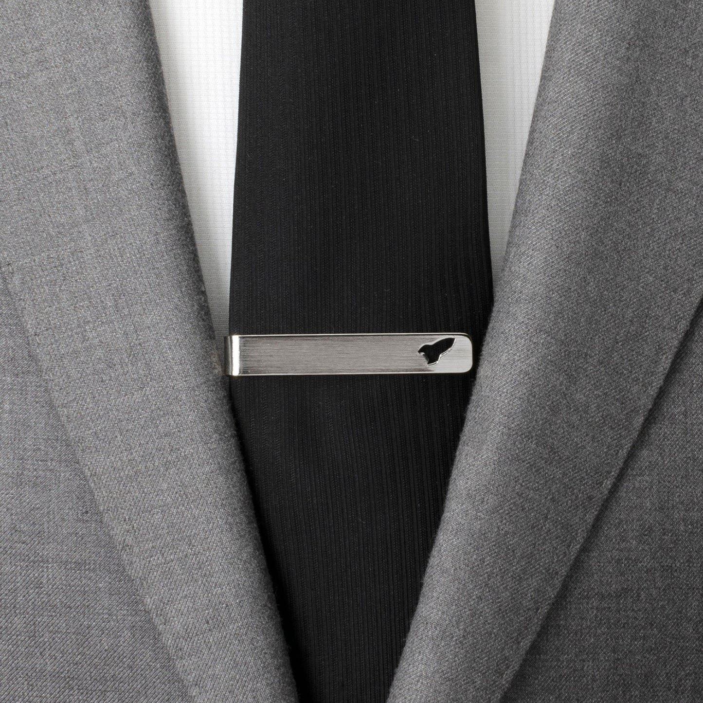 Close-up of a gray suit jacket with a black tie and silver tie clip.