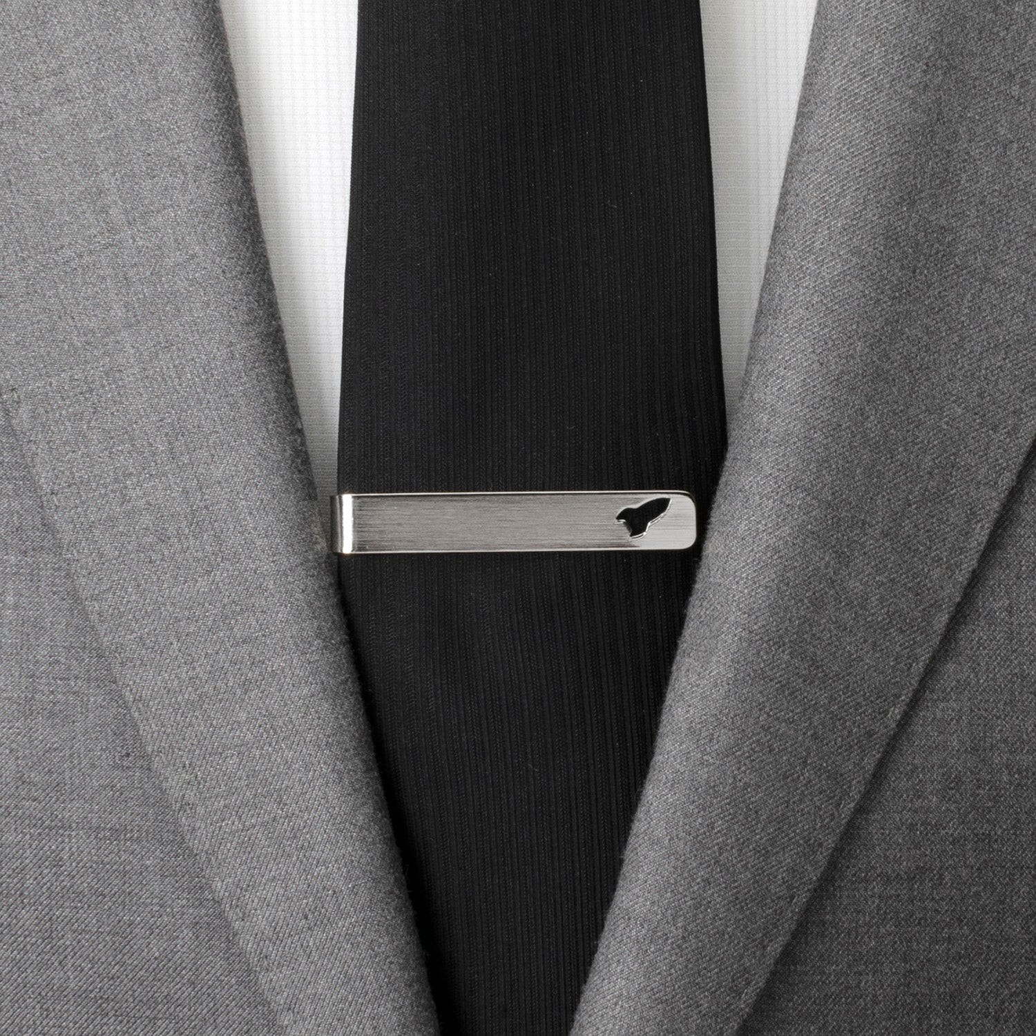 Close-up of a gray suit jacket with a black tie and silver tie clip.