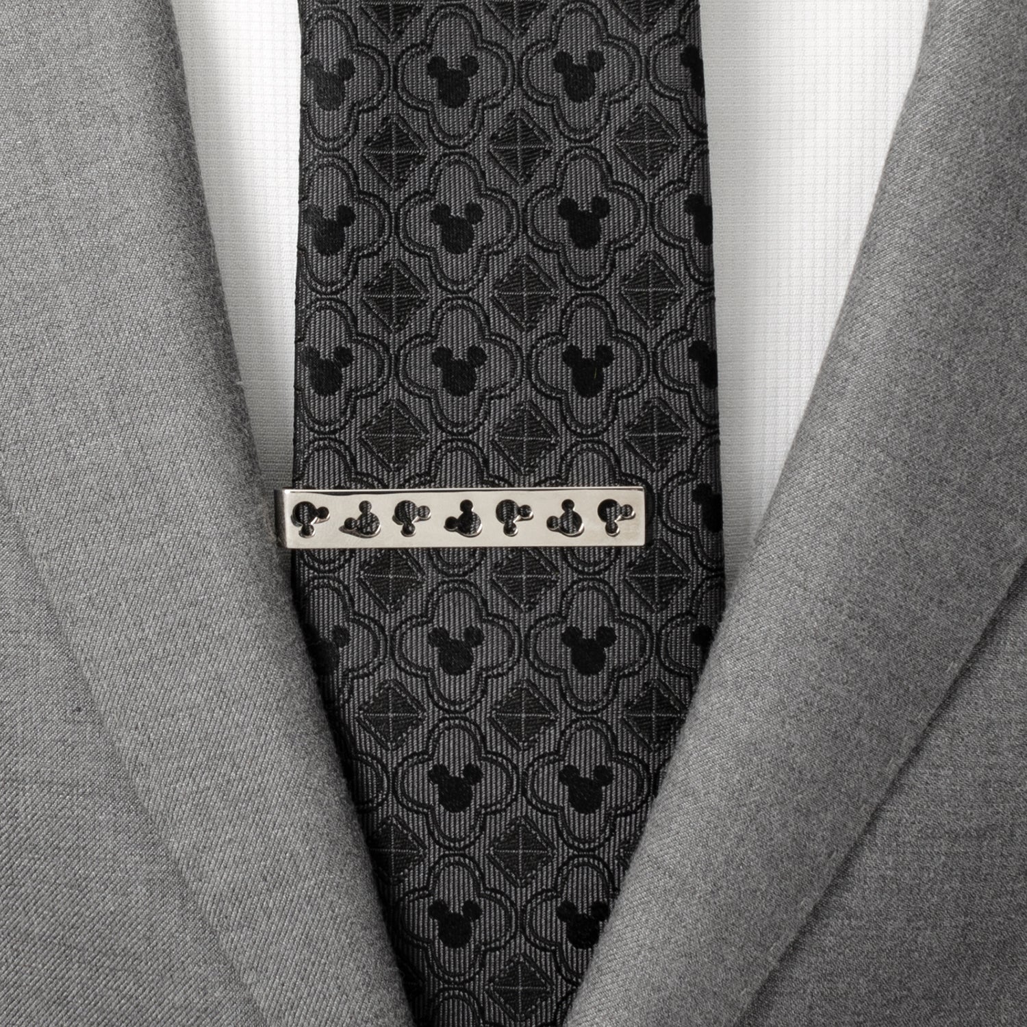 Gray suit jacket with a patterned tie and silver tie clip on a white shirt. Disney Mickey Mouse Silhouette Cutout Silver Tie Bar