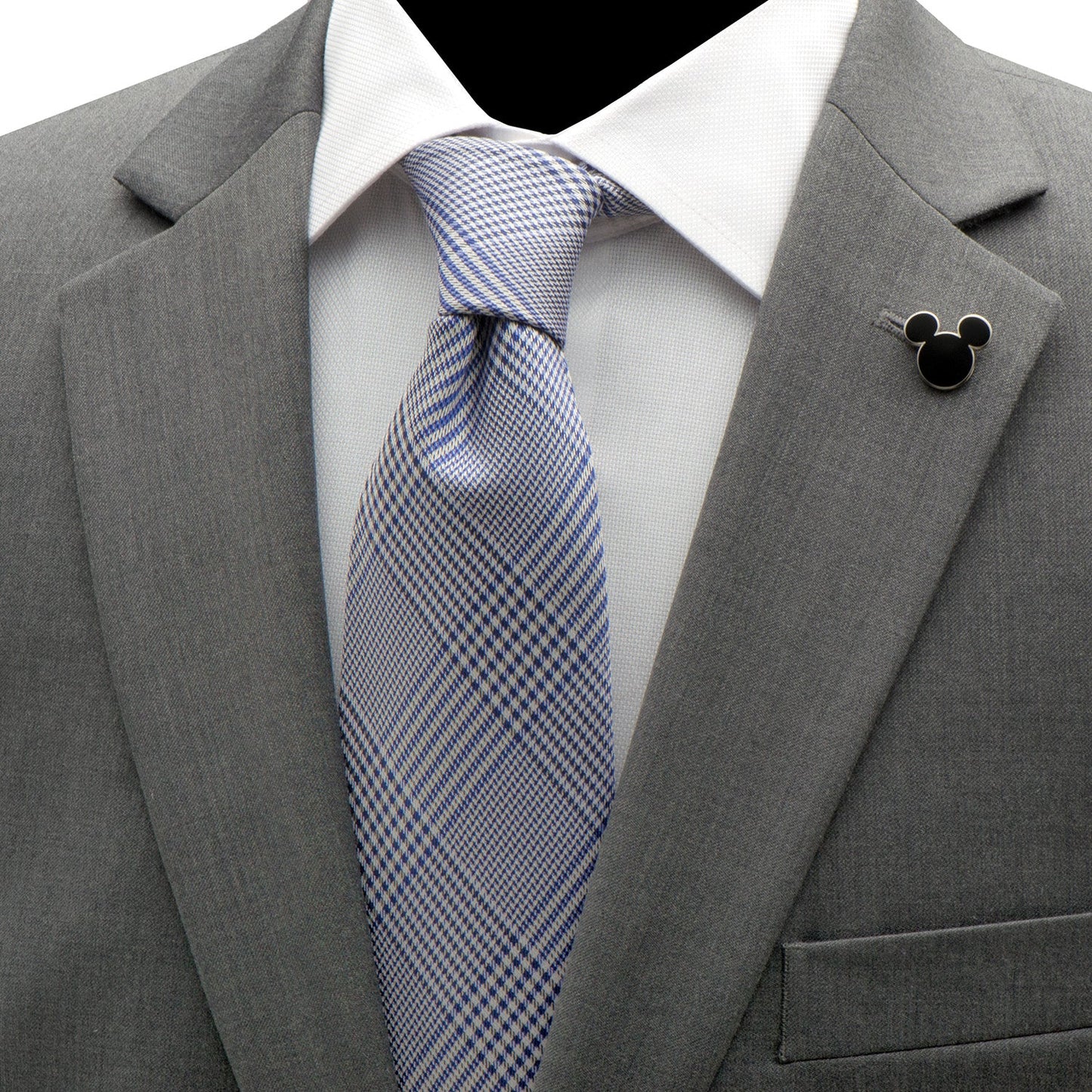 Gray suit jacket with a blue checkered tie and a black lapel pin on a white shirt.