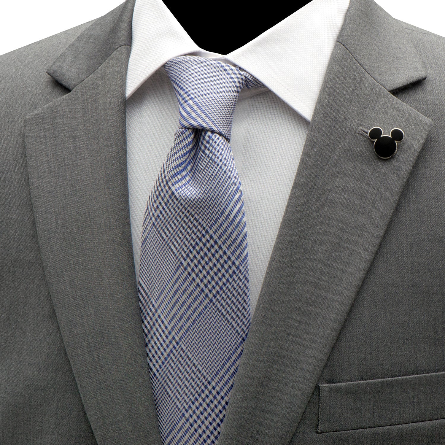 Gray suit jacket with a blue checkered tie and a black lapel pin on a white shirt.