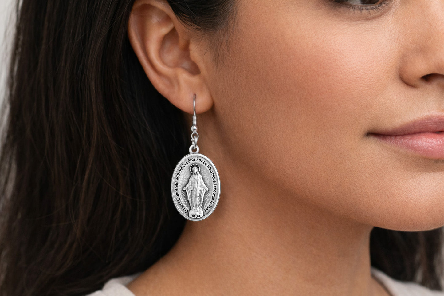 Close-up of a woman wearing a silver earring with a religious design.