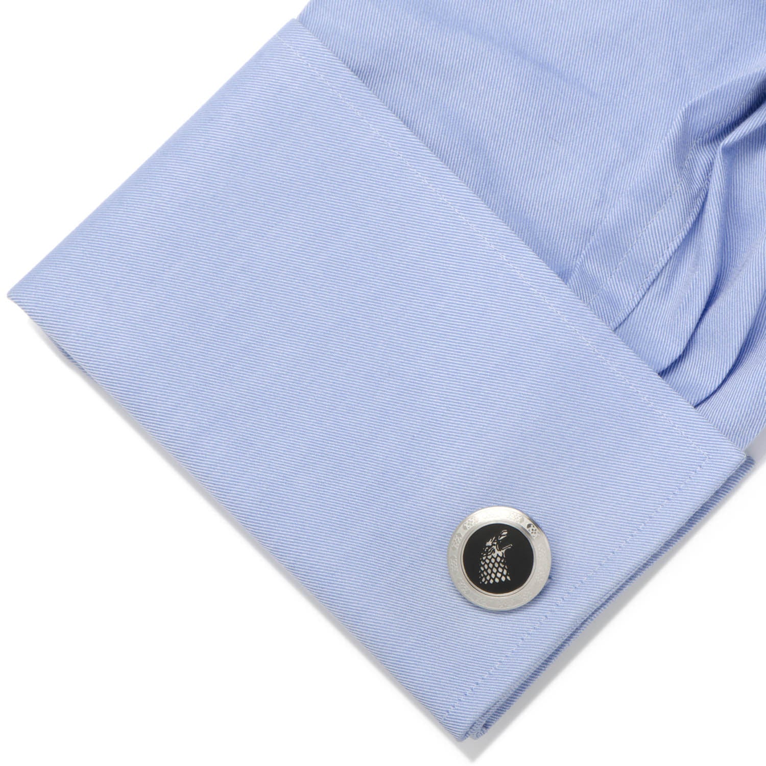 Close-up of a light blue shirt cuff with a silver cufflink featuring a black emblem.