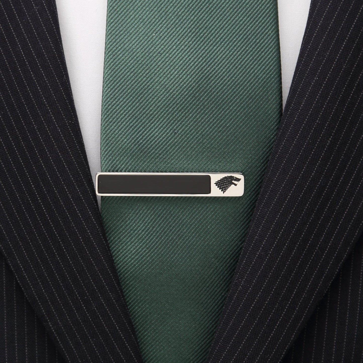 Green tie with a silver tie clip featuring a logo on a black pinstripe suit.