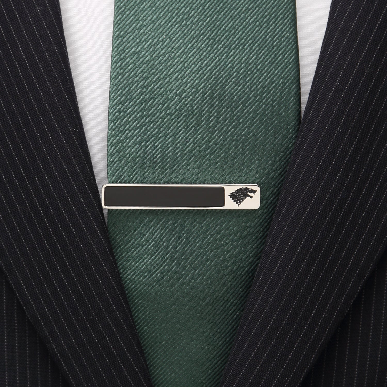 Green tie with a silver tie clip featuring a logo on a black pinstripe suit.