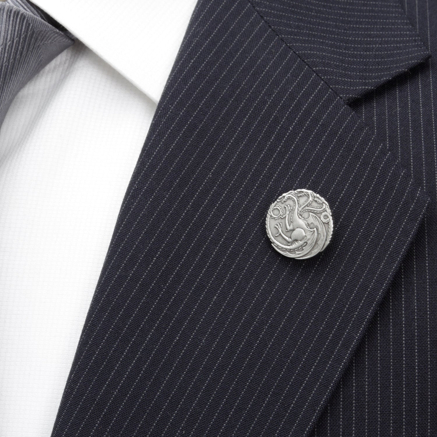 Close-up of a dark pinstripe suit jacket with a silver emblem on a white background