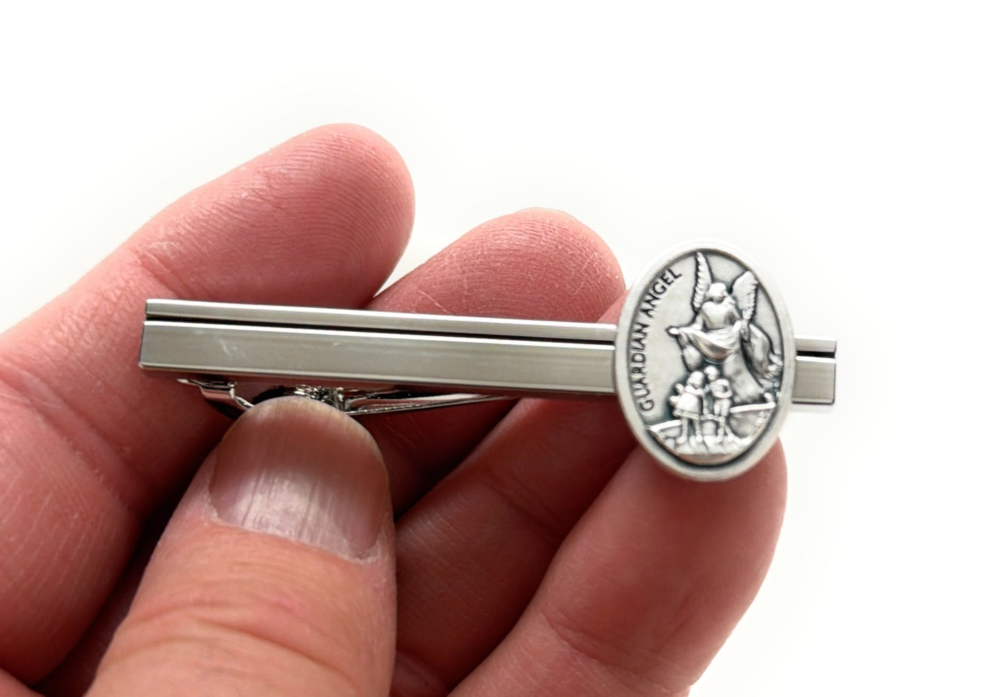 Silver tie clip with a detailed emblem held between fingers on a white background